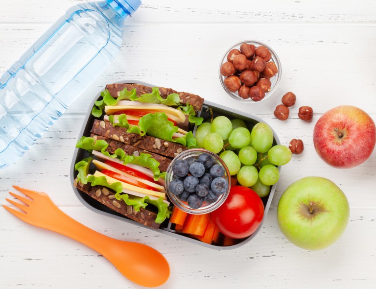 Healthy school lunch box with sandwich and fresh vegetables, water bottle, nuts and fruits. Top view flat lay
